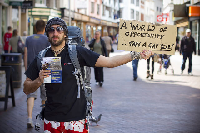 A man holds a sign that reads a world of opportunity... take a gap year! 
source:  4Tests