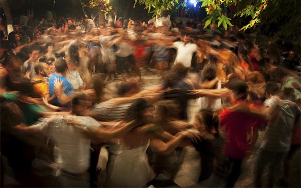 Ikaria natives and tourists dance closely together at a festival.